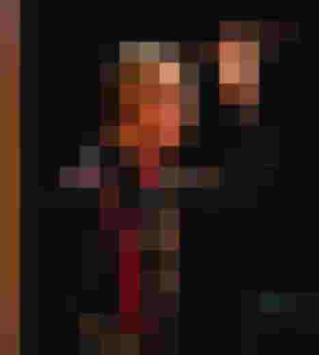 Dirigent mit Schlägel, schwarze Kleidung und rote Hosenträger bei einer musikalischen Darbietung.